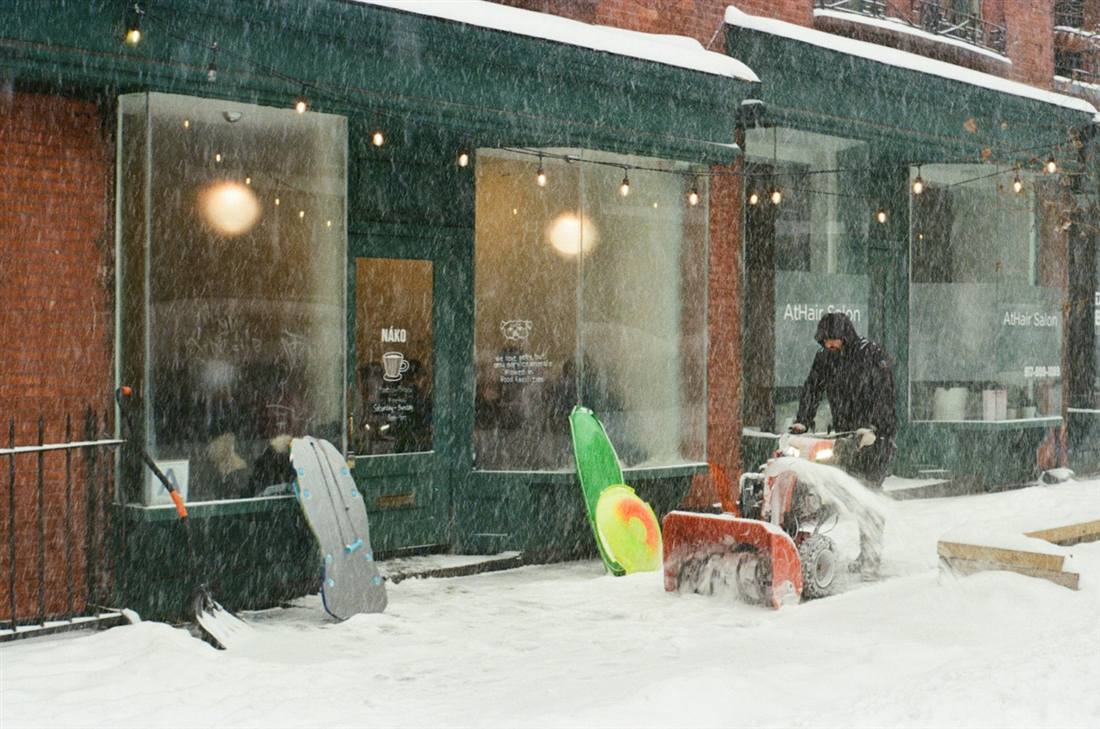 Worker clearing snow with a snowblower outside a storefront